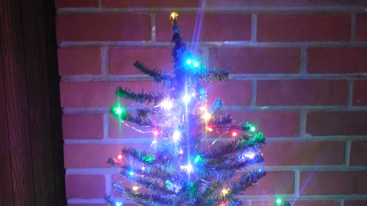Árbol de Navidad pequeño decorado con luces LED de colores junto a una pared de ladrillo