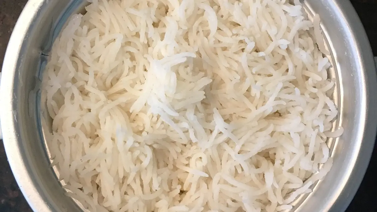 Arroz branco soltinho recém-cozido dentro do recipiente metálico de uma panela de arroz elétrica