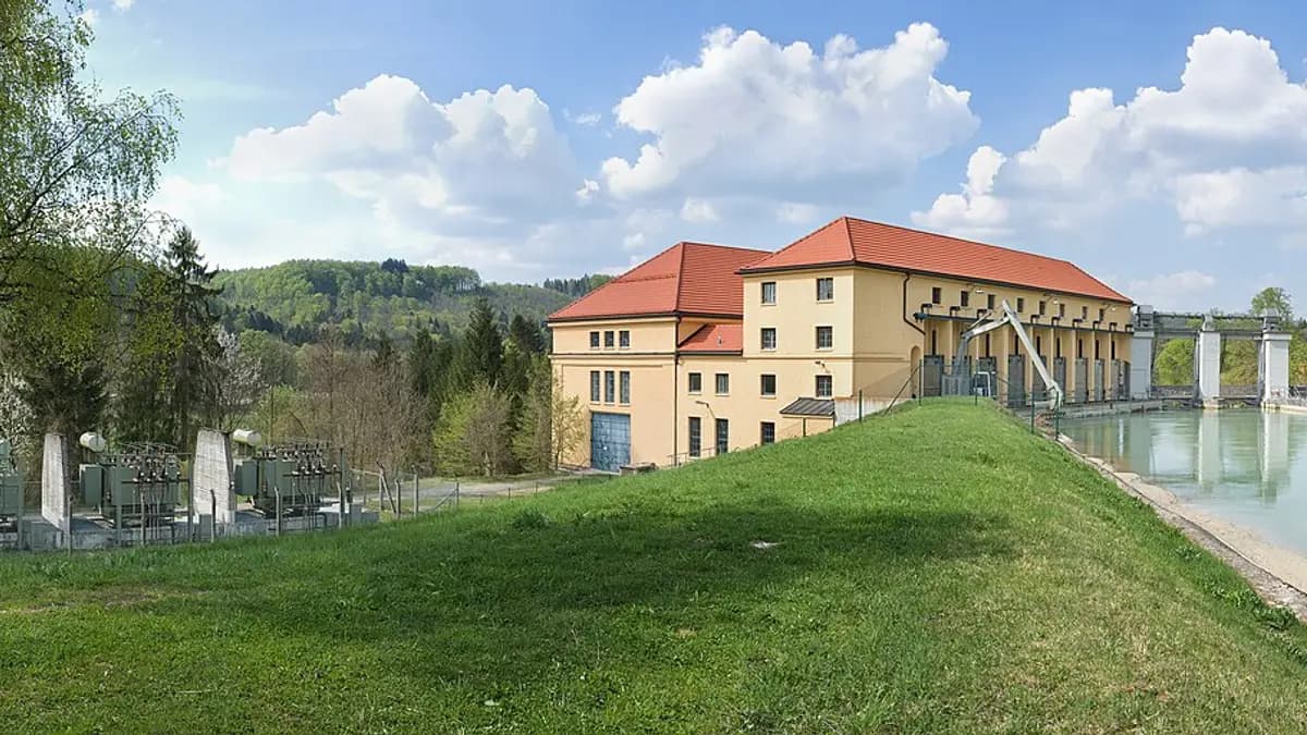 Edificio de una central hidroeléctrica de pasada junto a un río, con un prado verde delante