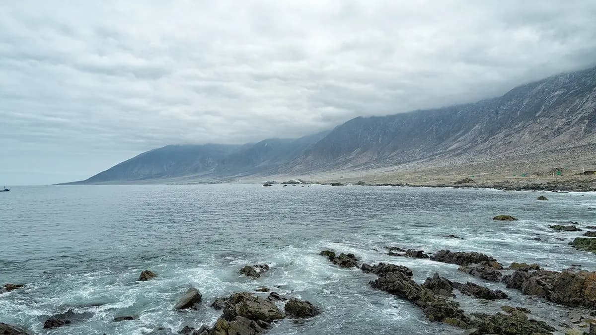 Litoral rochoso de Taltal com morros do deserto do Atacama ao fundo sob céu nublado