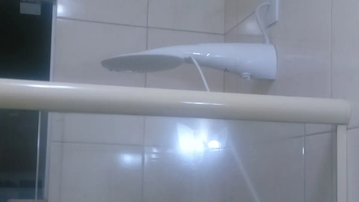 Chuveiro elétrico branco instalado na parede de um banheiro com azulejos brancos