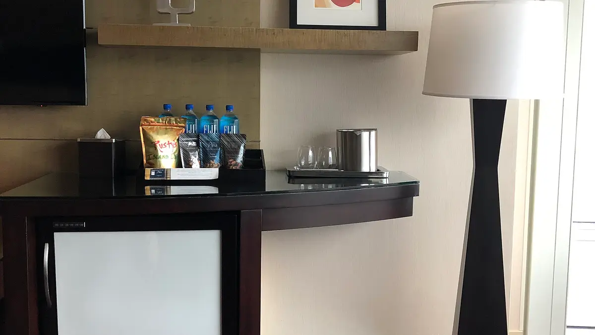 Hotel room with a white mini fridge under a counter and water bottles on top