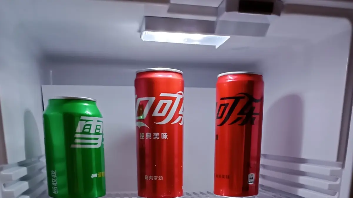 Lit interior of a mini fridge with three drink cans on a shelf