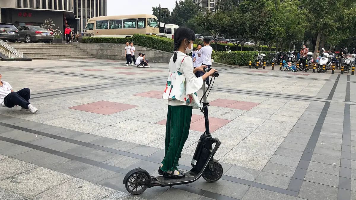 Uma jovem conduz um patinete elétrico em pé em uma praça de pedestres