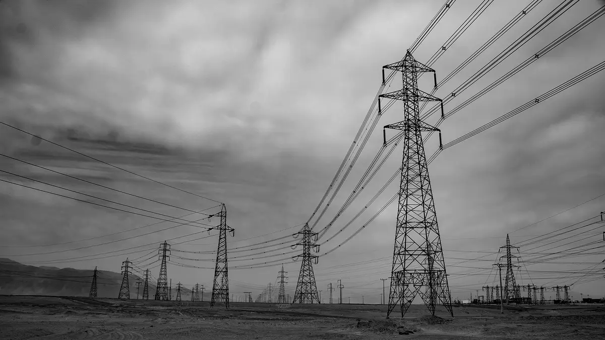 High-voltage towers and lines in the Mejillones desert under a cloudy sky