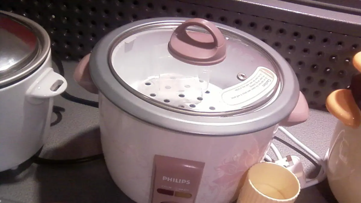 Panela de arroz elétrica branca com tampa de vidro e bandeja para cozinhar no vapor, numa vitrine