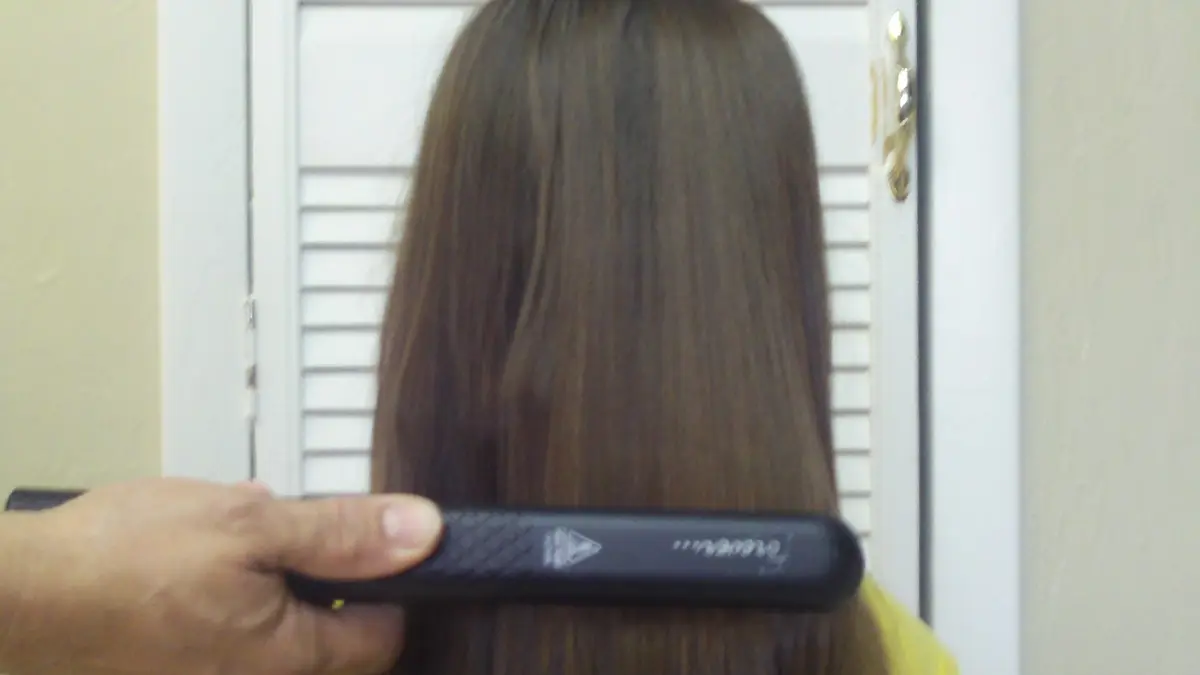 Mano que pasa una plancha de pelo negra por un cabello largo y castaño