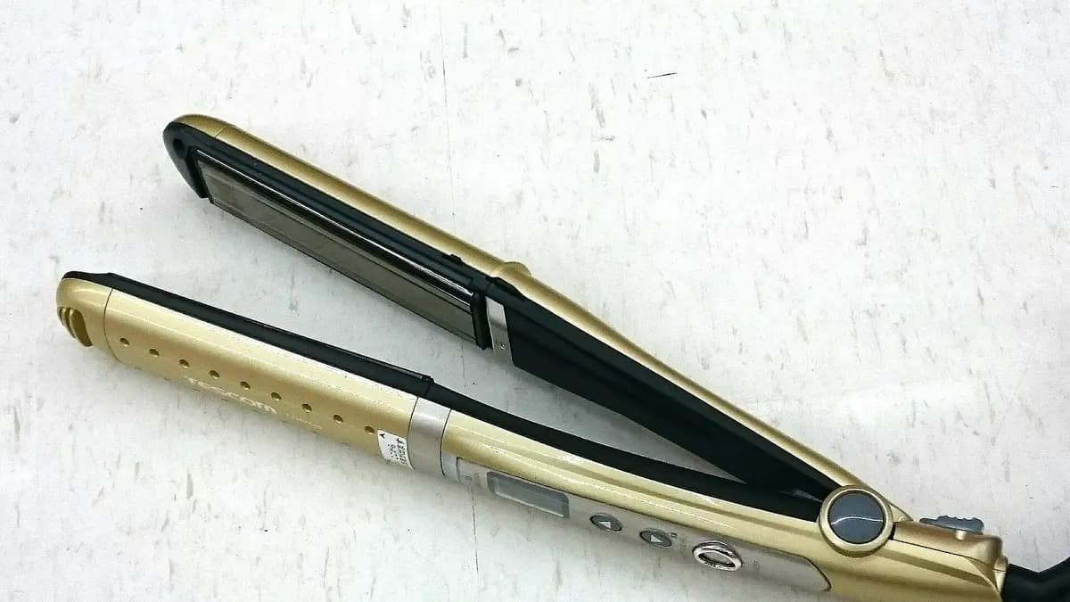 Plancha de pelo dorada y negra con pantalla digital sobre una superficie blanca