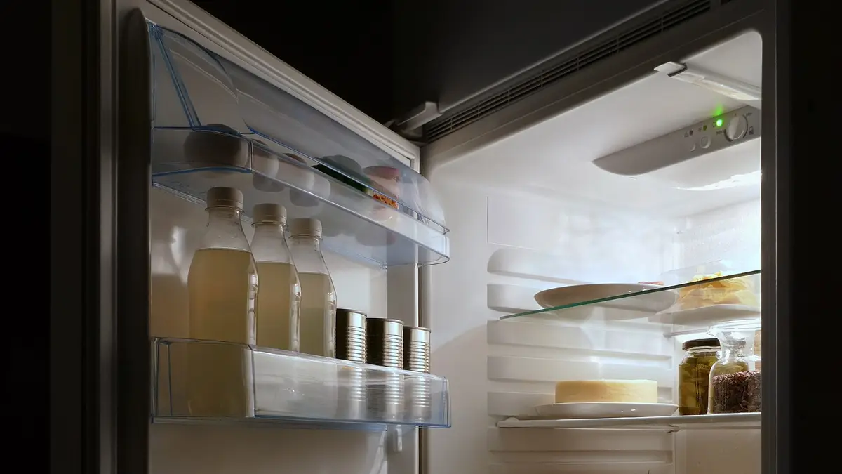 Refrigerator open at night with the interior light on and food on the shelves