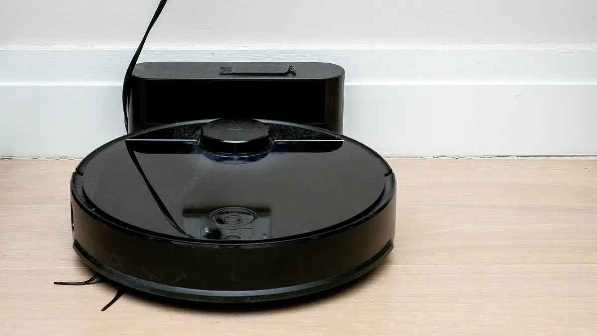 Black robot vacuum plugged into its charging base against the wall
