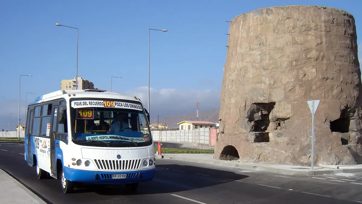 Un minibús diésel de la línea 109 de TransAntofagasta en una avenida de Antofagasta, junto a una antigua torre de piedra