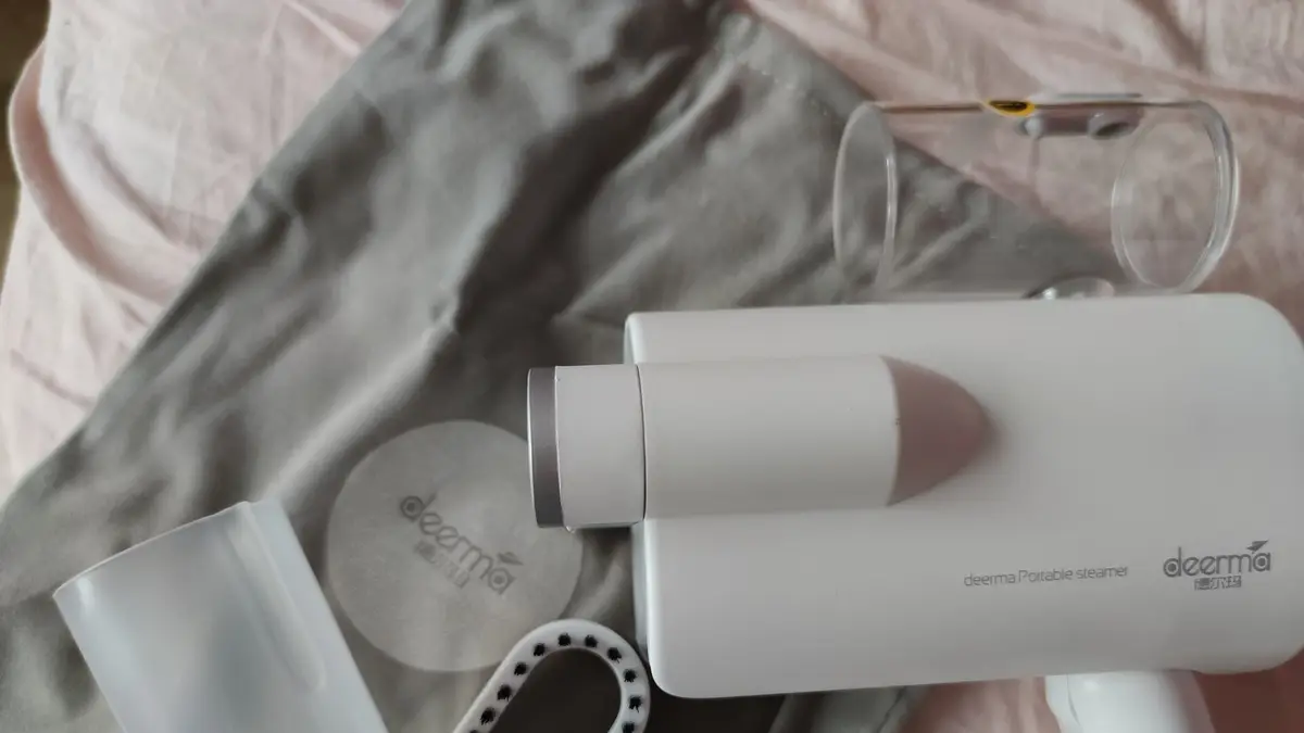 Vaporizador de roupa portátil branco sobre uma peça de roupa, com acessórios