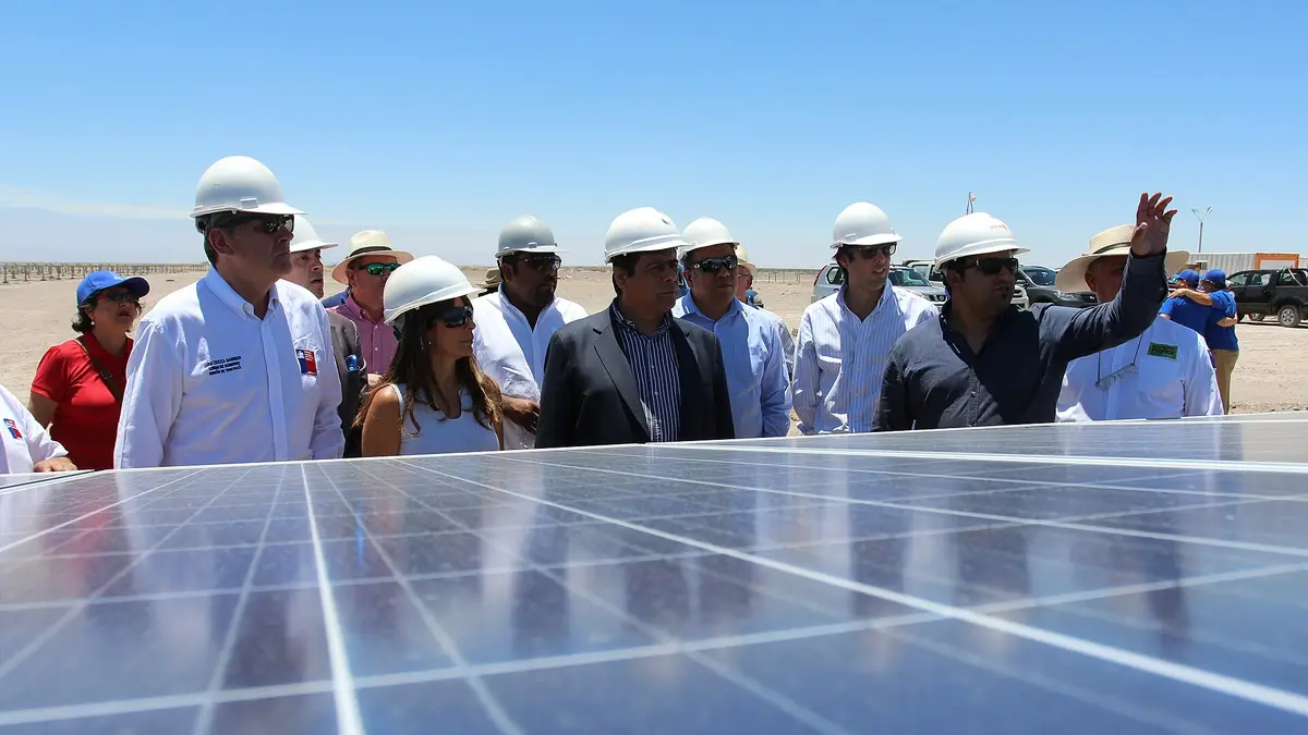 Visitors in white helmets next to a row of solar panels at the Pozo Almonte plant